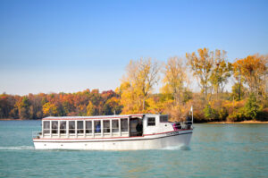 A boat named the Clinton cruises down the Detroit River and Lake St. Clair with trees in the background