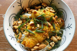 A white bowl with decorations holding Vietnamese turmeric fish with dill