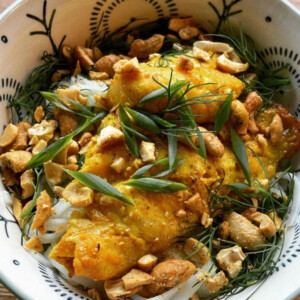 A white bowl with decorations holding Vietnamese turmeric fish with dill