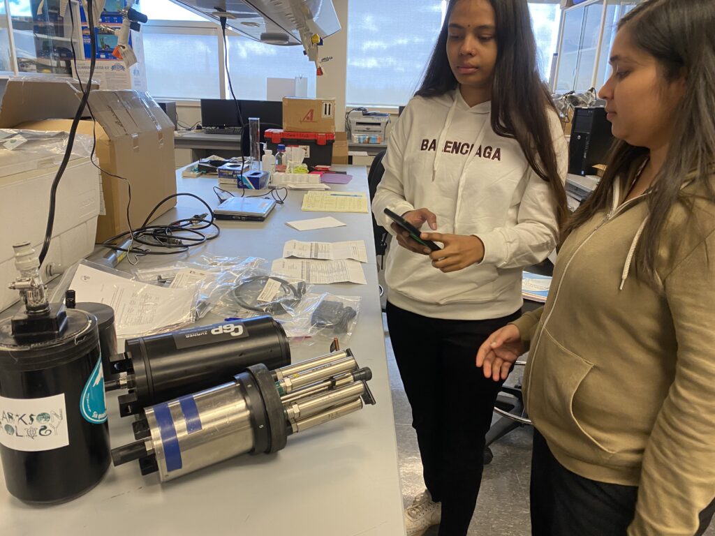 Two female students stand next to a lab bench with a bread-loaf-sized sensor array.
