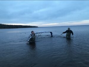 Two silhouetted figures stand waist-deep in water holding sampling tools