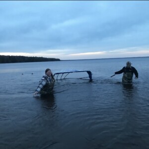 Two silhouetted figures stand waist-deep in water holding sampling tools