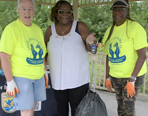 3 people holding a garbage back from the clean up event