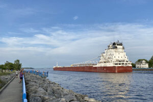 A freighter heading into a Lake from a channel with a boardwalk along the left side.