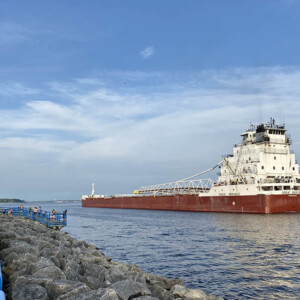 A freighter heading into a Lake from a channel with a boardwalk along the left side.