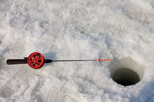 Ice fishing pole laying on a snowy lake next to a drilled round hole.