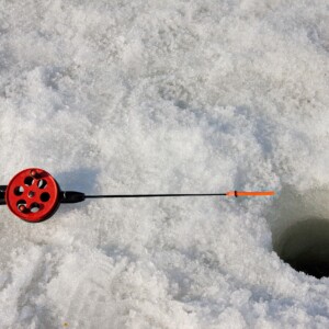 Ice fishing pole laying on a snowy lake next to a drilled round hole.