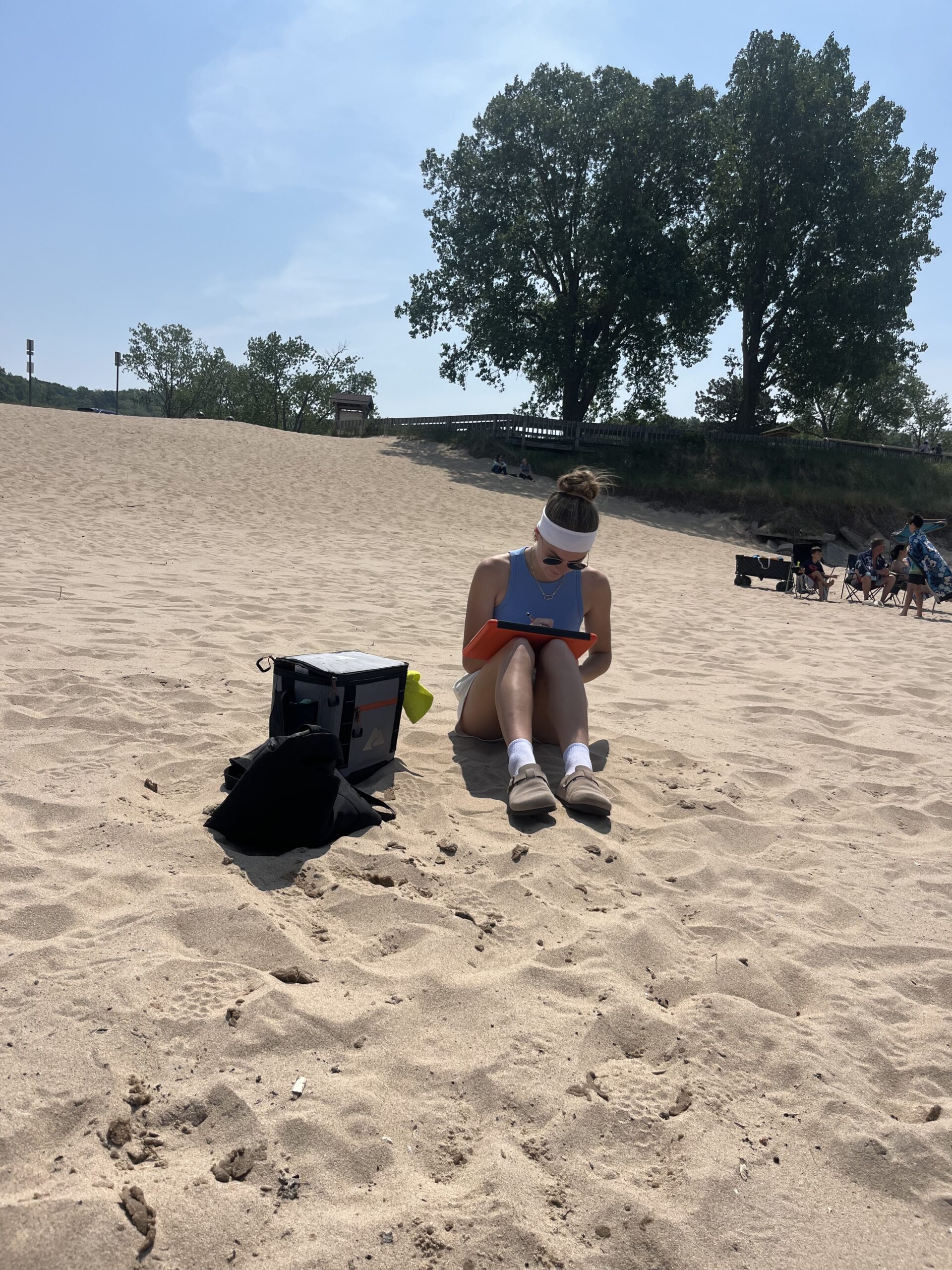 Annie sits on a sandy beach, taking notes