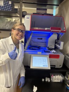 Annie stands next to a large square lab device