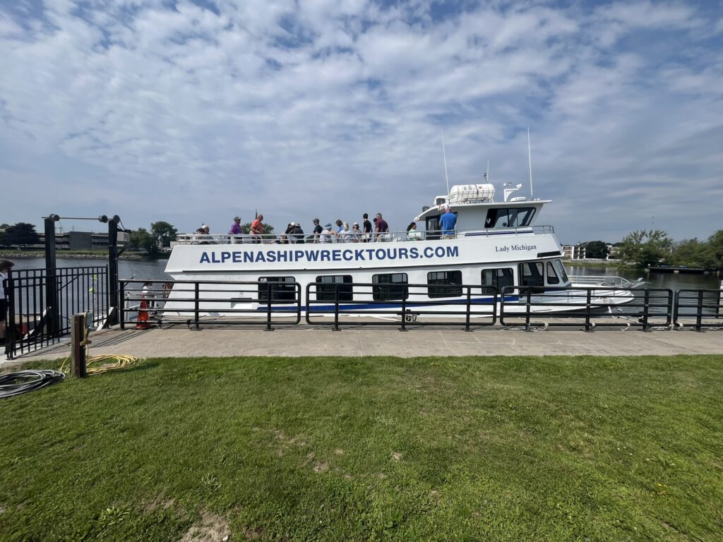 A glass bottom tour boat docked on the boardwalk readying to tour Lake Huron shipwrecks