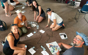 Five educators sit on the floor constructing the lakes from the lesson "How Well Do You Know the Great Lakes?"