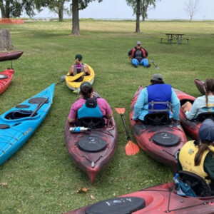 People in Kayaks on a park lawn near the shoreline, learning about kayak safety