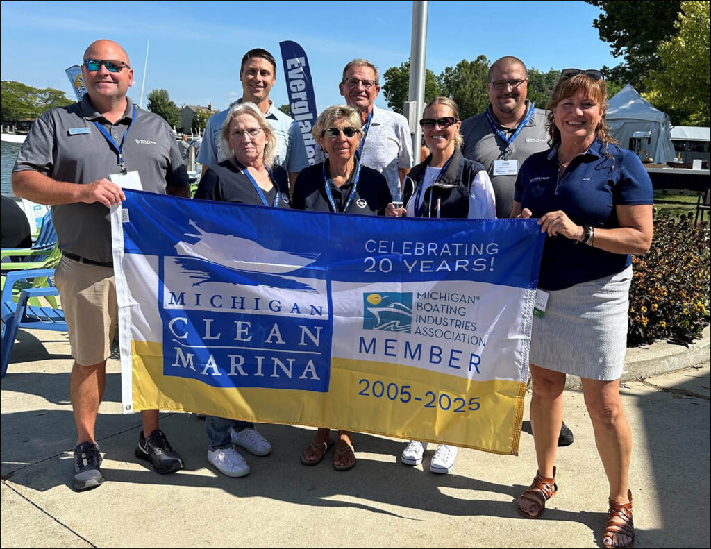 A group of marina reps hold a large flag with a boat on it.