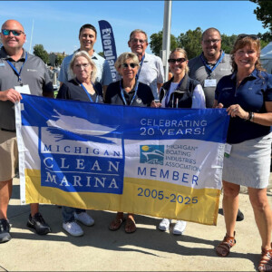 A group of marina reps hold a large flag with a boat on it.