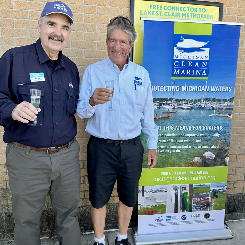 Two people celebrating the 20th year of the program standing by a Clearn Marina banner