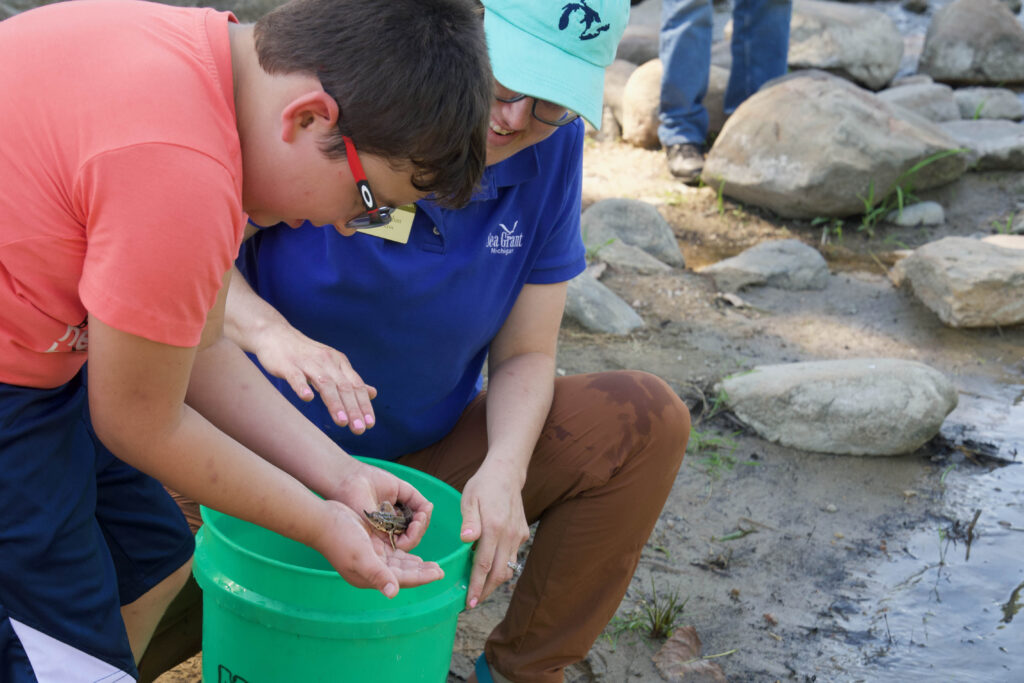 Two people help release a young lake sturgeon into a river