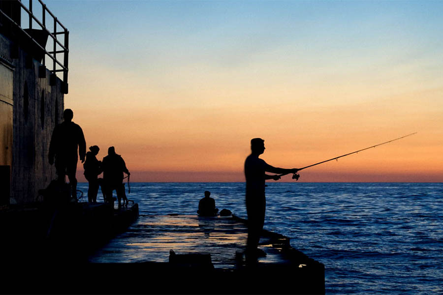 a person fishing off a pier at a great lake. sunset in the background