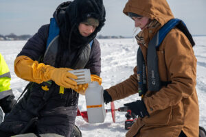 Two students on a frozen lake collect water samples