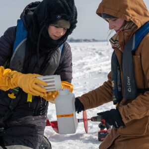 Two students on a frozen lake collect water samples