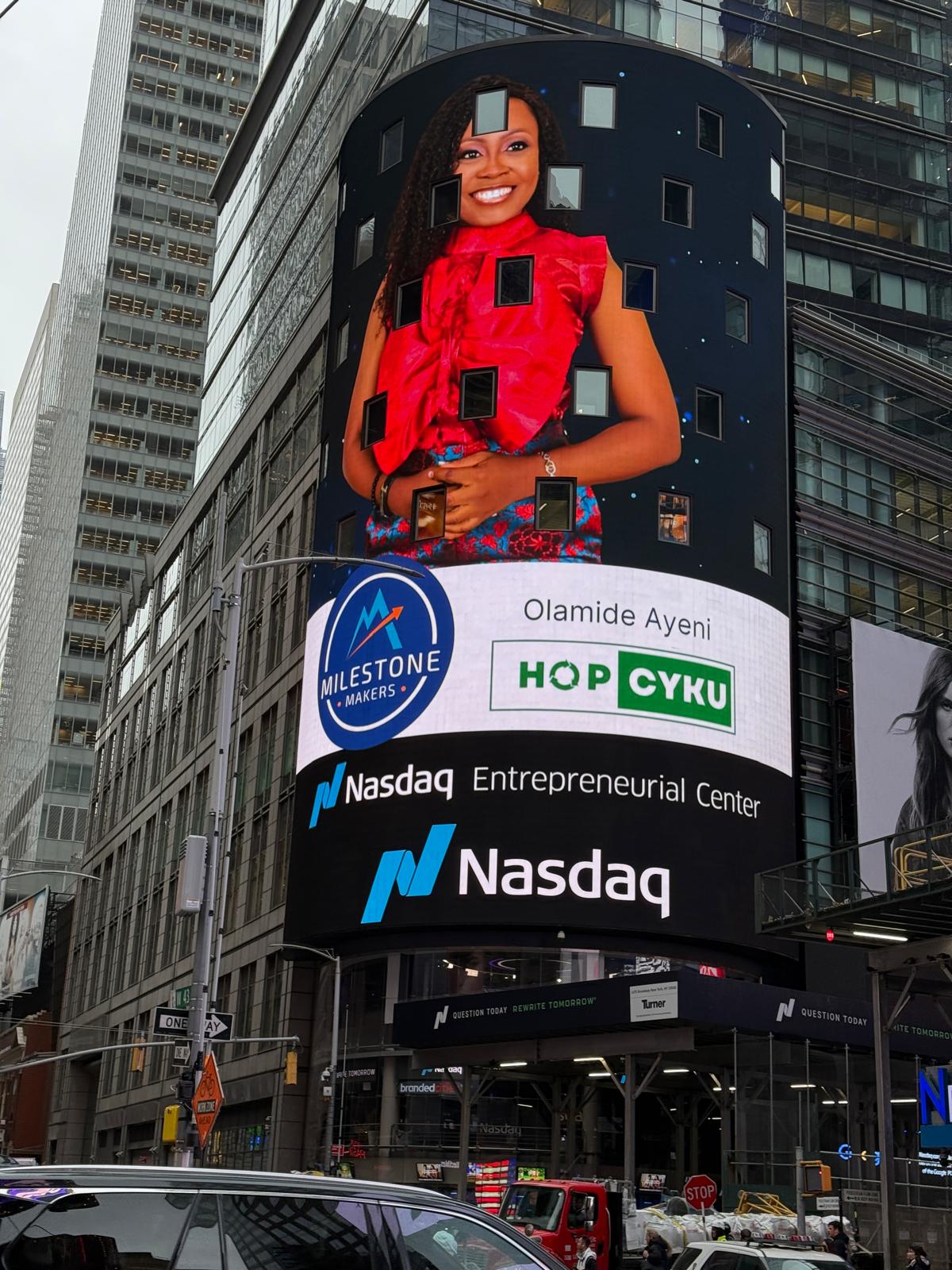 Ola Ayeni, a Black woman in a red dress, smiles from a billboard on a building in Times Square