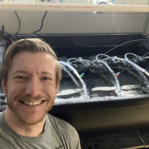 Researcher Scott Jackson stands in front of research equipment with walleye inside