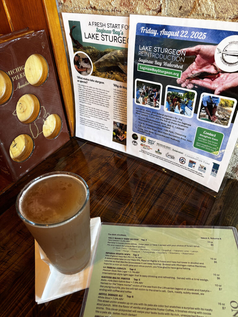 A pint of beer on a bar along with the menu, and two lake sturgeon release flyers