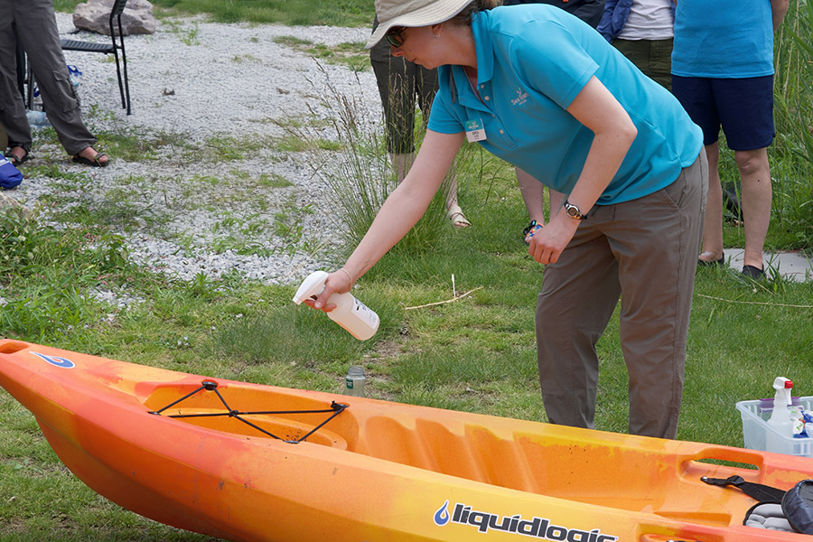 A person cleans their orange kayak with a spray bottle