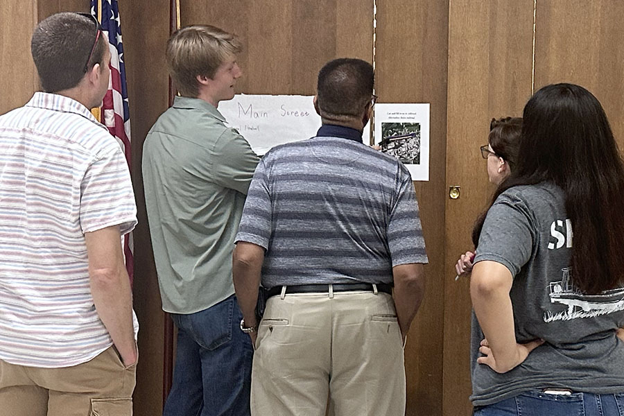a group of community members look at papers attached to a wooden wall that talk about their project