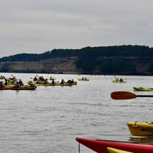 A very large group of kayaks on Lake Superior with Pictured Rocks National Lakeshore in the background on a cloudy day