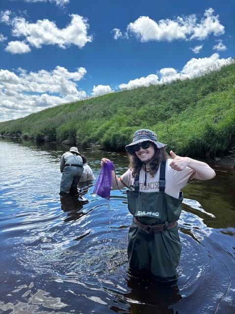 Simon and other researchers stand in a river under a blue sky